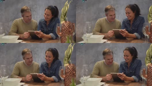 一对幸福的夫妇坐在家里的餐桌上一边聊天一边用平板电脑在网上购物高清在线视频素材下载