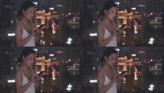 年轻漂亮的亚洲女人晚上在窗边用手机高清在线视频素材下载