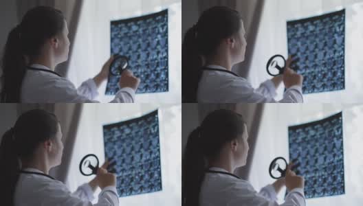聪明的白人年轻医生用放大镜分析大脑x光。集中美丽的黑发女人检查伦琴站在窗户在医院室内。高清在线视频素材下载