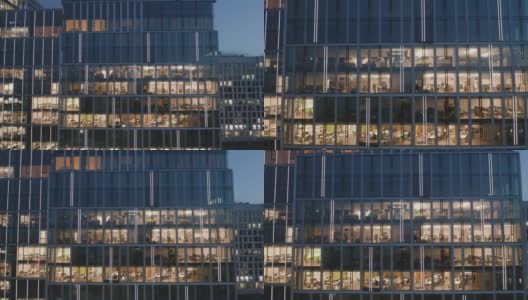 一架无人机向一幢夜间摩天大楼的窗户射击，办公室和商务人员在电脑前工作到很晚。高清在线视频素材下载