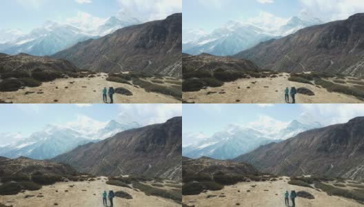一对夫妇在尼泊尔喜马拉雅山Annapurna马戏团徒步旅行的Manang山谷，在Annapurna链和Gangapurna的景色。干燥和荒凉的景观。白雪覆盖着高耸的山峰。高清在线视频素材下载