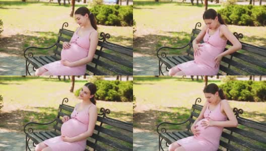 一个怀孕的女孩坐在公园的长椅上，她的胃开始疼痛，她开始正确地呼吸。孕妇抚摸着肚子高清在线视频素材下载