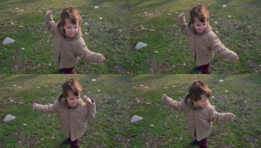 小男孩穿着温暖的夹克，在绿色的草坪上挥手跳舞高清在线视频素材下载