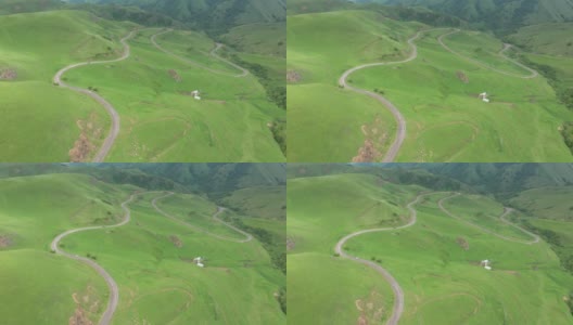 从山顶俯瞰穿过群山的山路。无人机拍摄到一条蜿蜒的道路穿过绿色的山丘和山脉。高清在线视频素材下载