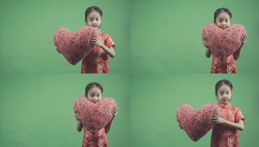 亚洲小女孩抱着孤立的心枕在绿色背景上，慢动作拍摄高清在线视频素材下载