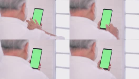 亚洲老爷爷在家看智能手机绿屏，用智能手机进行视频会议。家庭，高级卫生技术，医疗，退休，电子学习，医学和保健。绿色屏幕手持智能手机高清在线视频素材下载