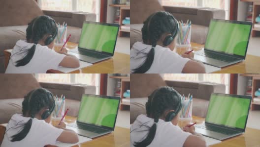 亚洲女童学生戴上耳机，通过视频电话与老师在线学习。由于Covid - 19大流行，在隔离期间，孩子正在用电脑笔记本电脑在家学习。高清在线视频素材下载