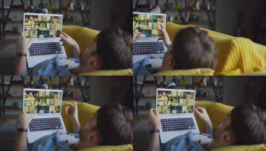 这是一个年轻人在家里的沙发上用笔记本电脑和一群同事或商业伙伴进行视频会议的照片高清在线视频素材下载