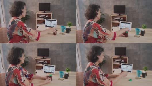 远程医疗的亚洲老年患者女性使用笔记本电脑视频电话与女医生，护士在家里的客厅高清在线视频素材下载