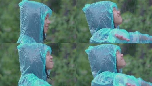 亚洲女孩穿着蓝色雨衣，喜欢下雨。孩子们在户外玩水花。缓慢的运动。高清在线视频素材下载