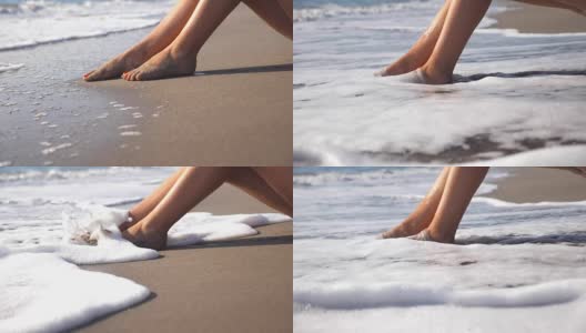 海浪冲刷着女性晒黑的脚。性感女孩的腿躺在海边的金色沙滩上，放松在暑假旅行。旅行的概念。慢动作关闭低角度视图侧视图高清在线视频素材下载