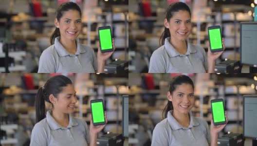 一个商店的女售货员拿着一部智能手机，屏幕上显示着对着摄像头微笑——色度键高清在线视频素材下载