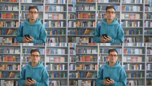一名年轻的千禧一代学生戴着眼镜，站在图书馆书架的背景下，用智能手机浏览社交网络信息高清在线视频素材下载