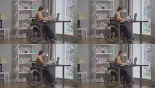 注意力集中的聪明残疾年轻妇女在轮椅上冲浪在笔记本电脑分析文件在室内的家庭办公室。宽镜头人像聪明的白人自由职业者工作在慢动作。高清在线视频素材下载