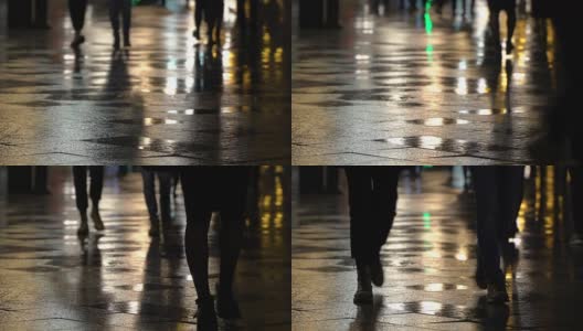 在潮湿的人行道上，街灯映出了辨认不出的人的剪影。长长的影子。雨夜的城市街道上有路灯，沥青路从雨中闪闪发光。不认识的行人，年轻人。夜晚的城市下雨。购物的概念高清在线视频素材下载