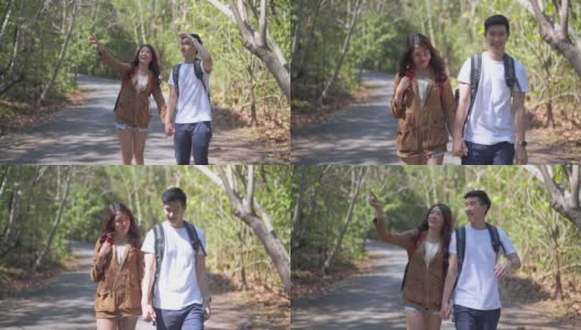 快乐的亚洲年轻情侣背着背包，在暑假里一起走在森林土路上的高清慢镜头。面带微笑的男女朋友喜欢在自然小道上徒步旅行。高清在线视频素材下载
