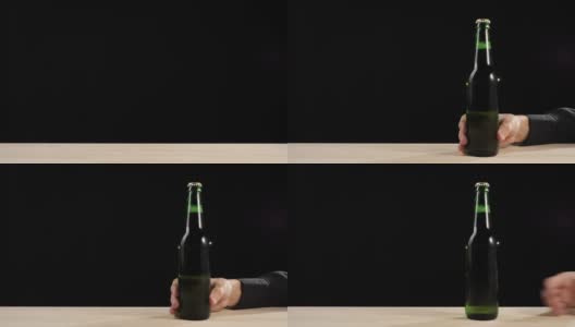 新鲜的啤酒。手拿着一瓶绿色的精酿啤酒在黑色背景的木桌上滑了进去。冰镇新鲜啤酒与水滴。准备饮料。广角镜头。4 k高清在线视频素材下载