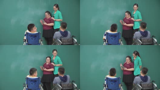 十几岁的唐氏综合症女孩练习演讲，在一个数字平板电脑上读演讲，残疾学生群体坐在轮椅上，亚洲美丽的女教师站在课堂上给予鼓励，感到幸福，积极的情绪。高清在线视频素材下载