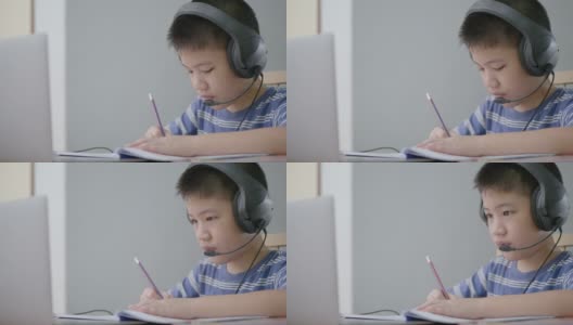新常态亚洲男孩学习在线看着屏幕笔记本电脑，在家里专心写作。技术教育的概念高清在线视频素材下载