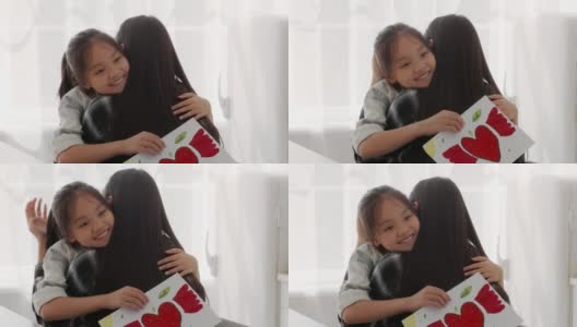 亚洲女孩抱着妈妈，手里拿着明信片祝贺家里的妈妈高清在线视频素材下载