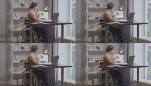 自信的白人年轻女子的肖像在轮椅上，在笔记本电脑视频聊天指着图表。美丽苗条的自由职业者工作消息在线从家庭办公室。远程工作的自由。高清在线视频素材下载