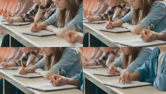 一排多民族学生在教室里考试的移动镜头。专注于拿笔和在笔记本上写作。聪明的年轻人在大学学习。高清在线视频素材下载