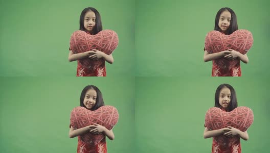 亚洲小女孩抱着孤立的心枕在绿色背景上，慢动作拍摄高清在线视频素材下载