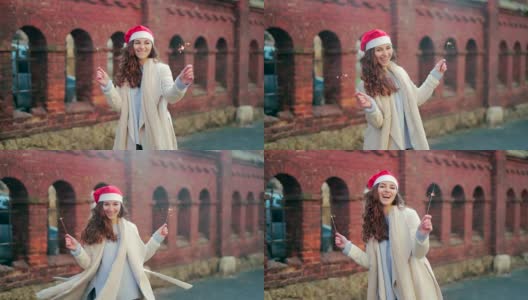 幸福的年轻女人的肖像，穿着大衣，戴着圣诞老人的圣诞帽，手里拿着烟花高清在线视频素材下载