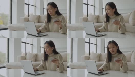 一个年轻的亚洲女人拿着信用卡，用着笔记本电脑。一位在家工作的女企业家。网上购物，在家工作的概念高清在线视频素材下载