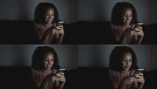 年轻女孩晚上在沙发上用手机发短信。镜头慢慢地靠近了她的脸。高清在线视频素材下载
