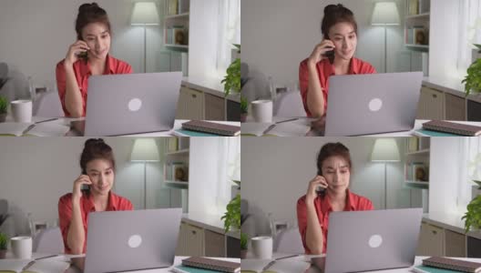 年轻漂亮的亚洲女性在家里用笔记本电脑工作，用智能手机聊天，面带微笑。女性在家工作时使用电脑和手机高清在线视频素材下载