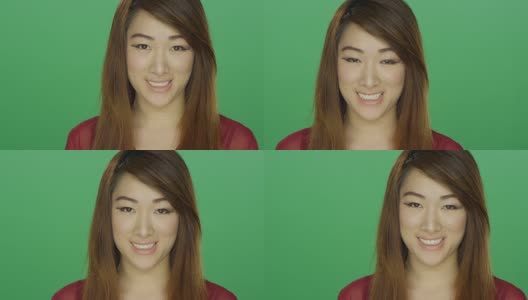 年轻的亚洲女人尴尬地微笑，在一个绿色屏幕的工作室背景高清在线视频素材下载