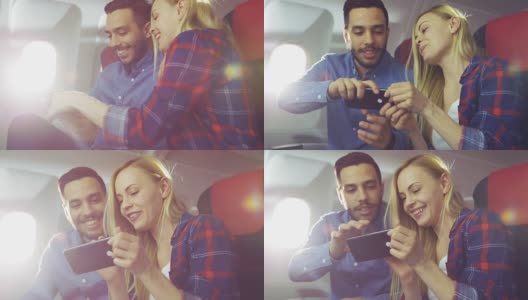 在一个商业飞机的董事会美丽的年轻金发英俊的西班牙男性看视频智能手机和微笑。阳光透过飞机窗户。高清在线视频素材下载