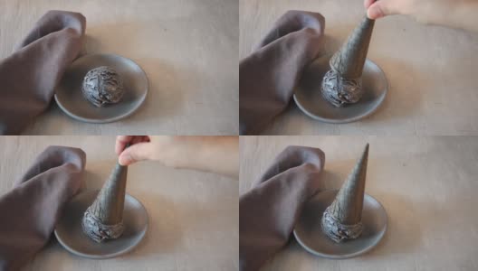 灰色的桌子上，灰色的陶瓷盘子上放着黑色的冰淇淋。女人的手把华夫蛋筒放在冰淇淋上。高清在线视频素材下载