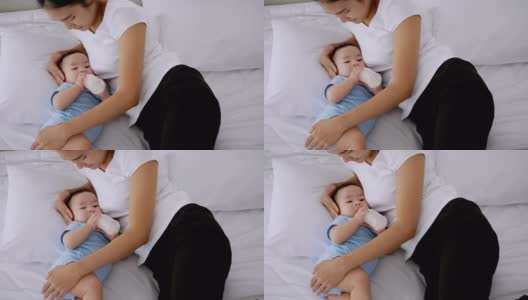 年轻的母亲在床上用奶瓶喂小婴儿。高清在线视频素材下载