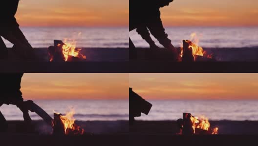 剪影人放置在海滩篝火上的原木高清在线视频素材下载