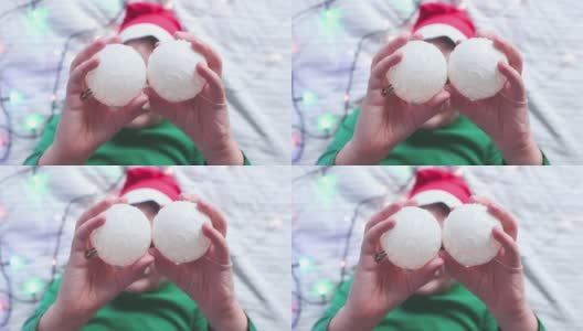 圣诞节装饰品的特写镜头:孩子们手中的白色闪光球。孩子躺着玩圣诞树球，开心地笑着。高清在线视频素材下载