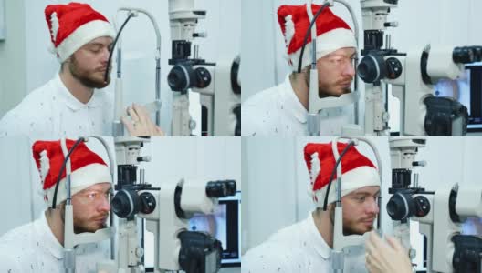戴圣诞帽的眼科病人。一个男人在诊所测试他的眼睛。年轻男性病人检查视力。高清在线视频素材下载