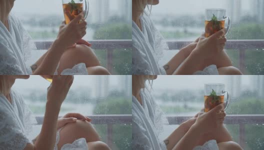 年轻女子享受着她的早茶，看着窗外的雨。美丽浪漫的陌生女孩在舒适的家里喝热饮。雨天的心情高清在线视频素材下载