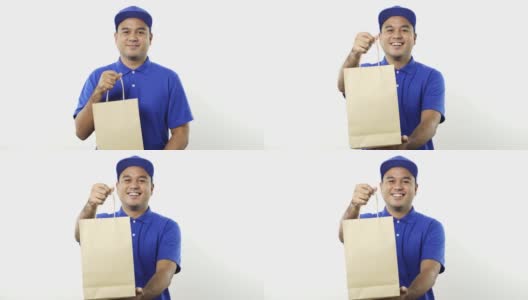 微笑年轻的亚洲快递员在蓝色制服给纸袋的客户在孤立的白色背景。4 k决议。高清在线视频素材下载