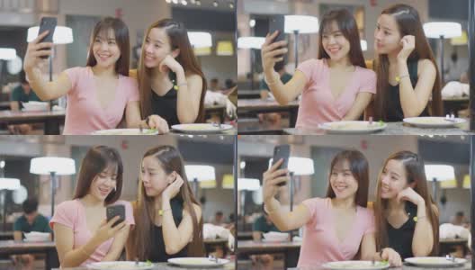 快乐两个年轻的亚洲女孩在餐厅用餐后一起用手机自拍。女人用智能手机看摄像头，然后捕捉到微笑。高清在线视频素材下载