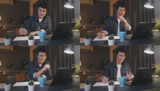 一名亚洲男子在家里工作到很晚，在视频电话会议中使用笔记本电脑，并在笔记本上写字高清在线视频素材下载