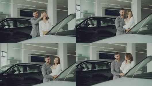 快乐的男人是让惊喜他的妻子闭上她的眼睛与他的手，并带领她到美丽的新车是汽车展厅，快乐的女人是拥抱和亲吻他。高清在线视频素材下载