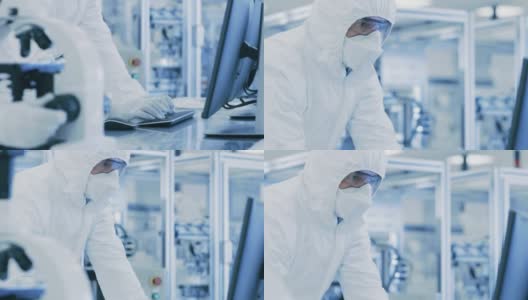 在实验室，科学家穿着防护服做研究，使用显微镜和输入数据到个人电脑。现代制造半导体和制药项目。高清在线视频素材下载