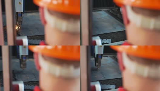 在工业企业里，金属零件是用激光切割机切割的一个身穿橙色制服的工人的前景轮廓高清在线视频素材下载