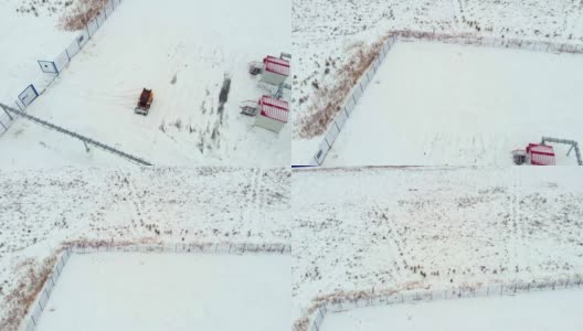一辆小型拖拉机装载机清理石油和天然气设备建筑附近的积雪。一架无人机在工业区内被雪覆盖的石油工厂和燃气轮机发电厂上空飞过高清在线视频素材下载