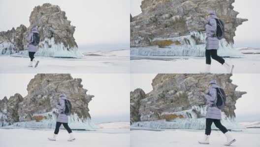 女人在贝加尔湖冰面上的旅行。冬岛之旅。女孩在冰岩石下行走。游客看着美丽的冰洞。极限跋涉和步行。背包客在大自然中休憩。高清在线视频素材下载