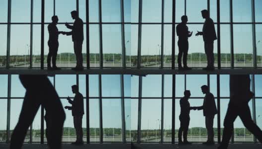 两个商人的剪影，握手和交谈站在办公大厅的大全景窗口，同事在慢镜头走过他们高清在线视频素材下载