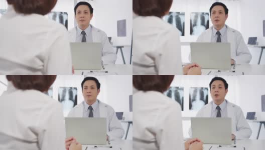 严肃的亚洲男医生正在用笔记本电脑传送好消息，谈论结果或症状与女病人坐在医院办公室的桌子前。高清在线视频素材下载