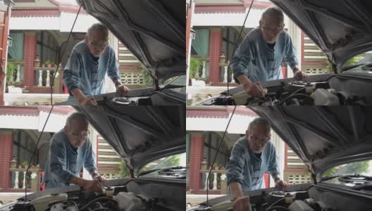 亚洲白发老人戴着眼镜，在家里清洗和检查他的旧车的发动机状况。老年人退休生活。高清在线视频素材下载